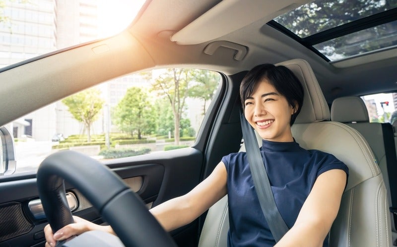 Smiling woman sitting in the driver’s seat while driving a car.