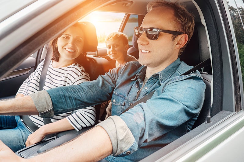 Smiling family sitting in a car and a man is driving.